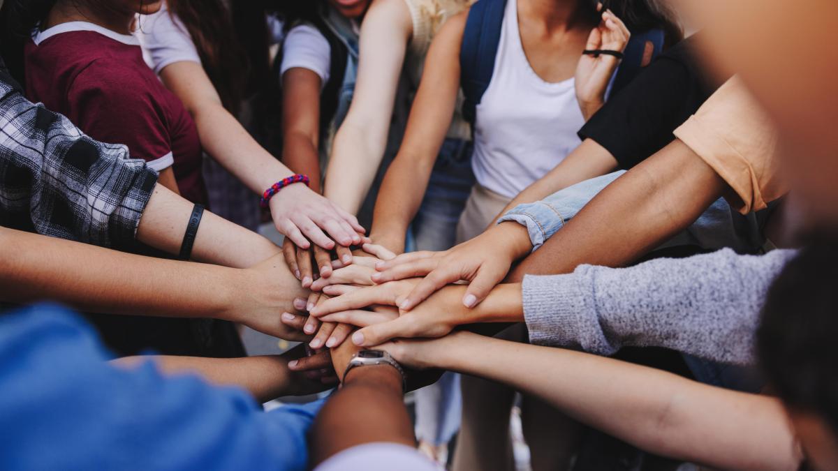 A group of diverse hands pile on top of each other in the center, symbolizing teamwork and unity.